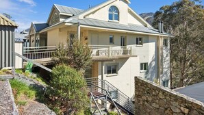 A two-story building with a balcony, a stone retaining wall, and a staircase leading to the entrance. - Inala 2 is an exceptional top floor, one bedroom and loft apartment. (Thredbo)