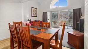 A dining area with a wooden table and chairs, a sofa, and a television. - Inala 2 is an exceptional top floor, one bedroom and loft apartment. (Thredbo)