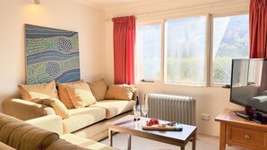 A living room with a sofa, a coffee table, a television, and a painting on the wall.
