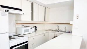 A modern kitchen with white cabinetry, a built-in microwave, a kettle, a stove, and a sink.