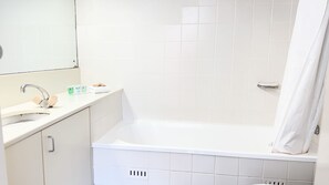 Une salle de bain avec un lavabo blanc, un miroir et une baignoire. On peut voir des articles de toilette sur le comptoir du lavabo.