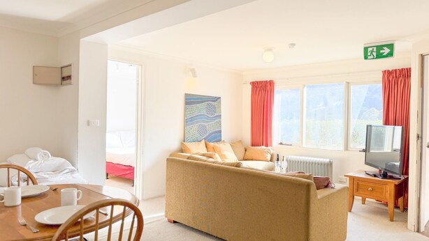 A well-lit room with a sofa, a dining table with chairs, a TV, and a painting on the wall.