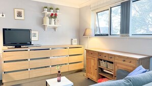 Un salon moderne avec un téléviseur, des meubles en bois, une petite table sur laquelle est posé un vase, et une fenêtre avec des rideaux.