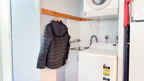 Une petite cuisine équipée d’un lave-linge, d’un évier et d’une étagère en bois située au-dessus du lave-linge.