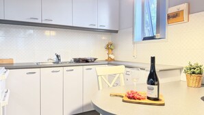 Une cuisine moderne avec des meubles blancs, un plan de travail en granit, une bouteille de vin et une planche à découper avec des raisins.