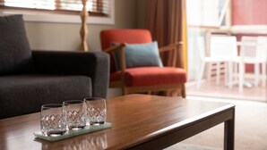 Ett modernt vardagsrum med ett soffbord i trä, tre genomskinliga glas, en mörkgrå soffa, en röd fåtölj och en lampa.