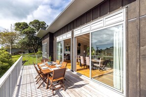 Una casa moderna con una terrazza in legno e ampie porte scorrevoli che si aprono su un'area pranzo all'aperto.