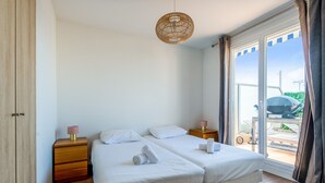 A double bed with white linens, a bedside table with a lamp, and a view of the outdoors through a sliding door. - La Terrasse Zéphyr - Welkeys (Antibes)