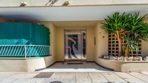 A building entrance with a metal gate, a door with a geometric design, and a small palm tree. - La Terrasse Zéphyr - Welkeys (Antibes)