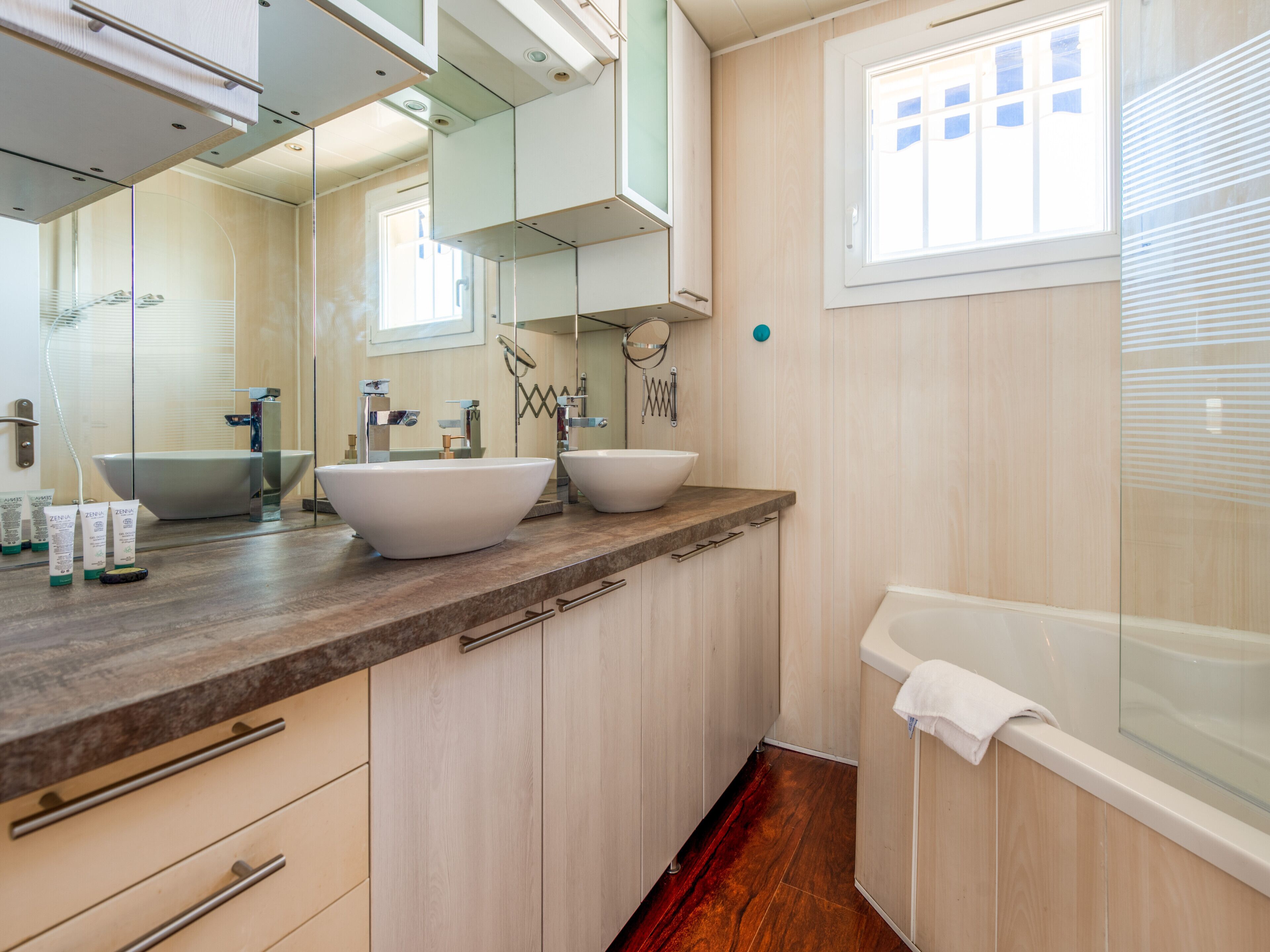 Un baño moderno con dos lavamanos grandes, una bañera y una ventana con persianas.