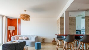 A modern living room with a grey sofa, a wooden dining table with chairs, a floor lamp, and a hanging light fixture. - La Terrasse Zéphyr - Welkeys (Antibes)