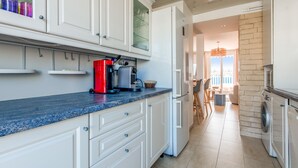 A modern kitchen with white cabinets, a red coffee machine, and a built-in washing machine. - La Terrasse Zéphyr - Welkeys (Antibes)