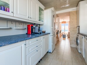 Uma cozinha moderna com armários brancos, uma máquina de café vermelha e uma máquina de lavar integrada.