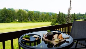 A table with cheese, crackers, and grapes on a balcony overlooking a grassy field and forested hills. - Summer Adventure Retreat - Golf Views, King Beds, Fully Loaded Kitchen! (Mancelona)