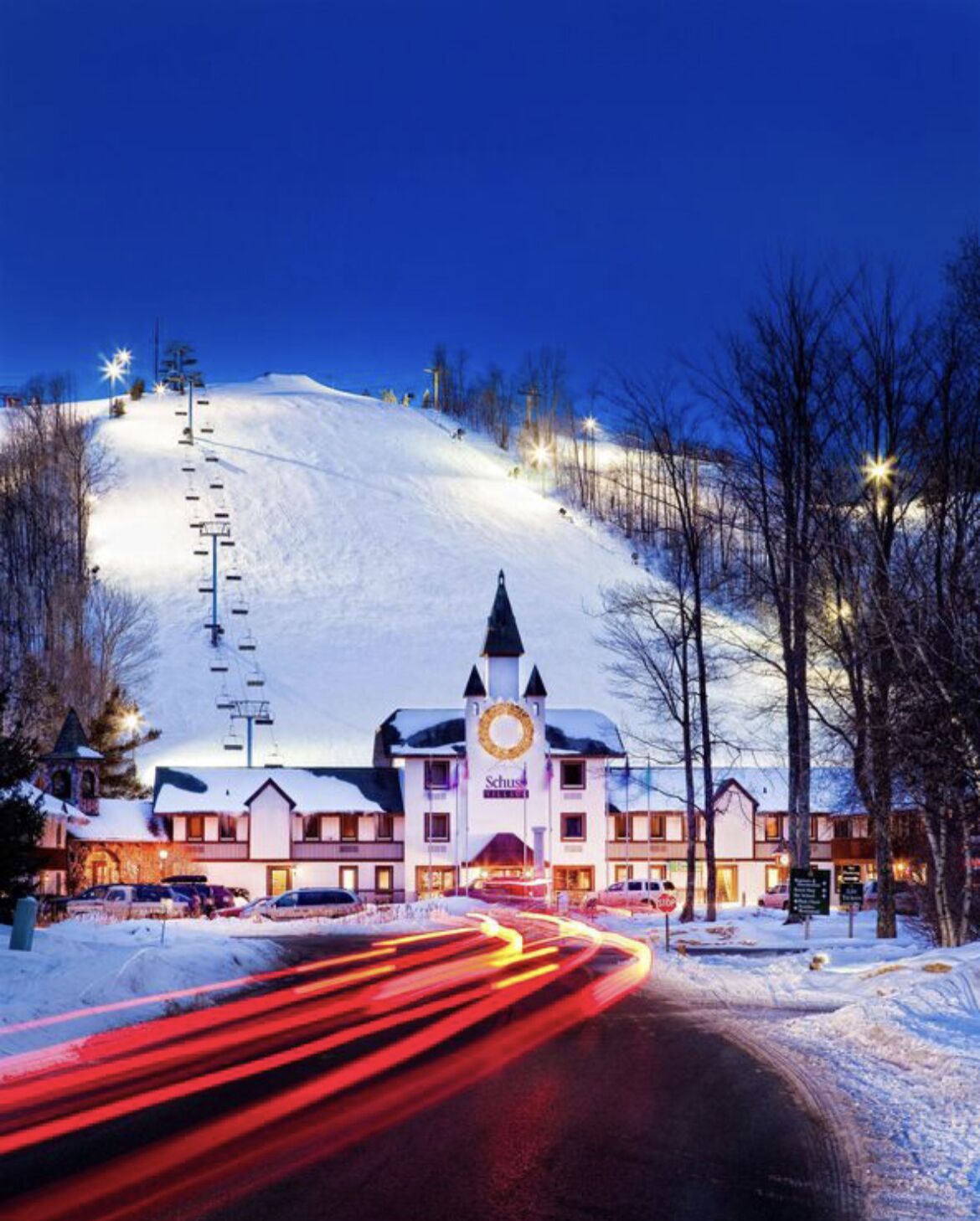 A hotel with a prominent clock tower, a ski lift in the background, and a snowy landscape. - Summer Adventure Retreat - Golf Views, King Beds, Fully Loaded Kitchen! (Mancelona)