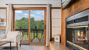 A cozy room with a fireplace, a sliding glass door to a deck, and a comfortable seating area. - Summer Adventure Retreat - Golf Views, King Beds, Fully Loaded Kitchen! (Mancelona)