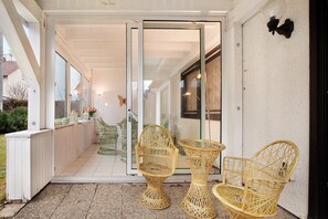 Ein überdachter Außenbereich mit Korbstühlen, einer Glastür und Blick ins Haus.