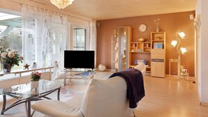 Ein modernes Wohnzimmer mit einem Glastisch, einem weißen Ledersofa, einem Fernseher und einer dekorativen Chandel.