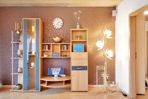 Ein modernes Zimmer mit einem Holztisch, einem Computer, einem Bücherregal, einer Uhr und einer dekorativen Stehlampe.
