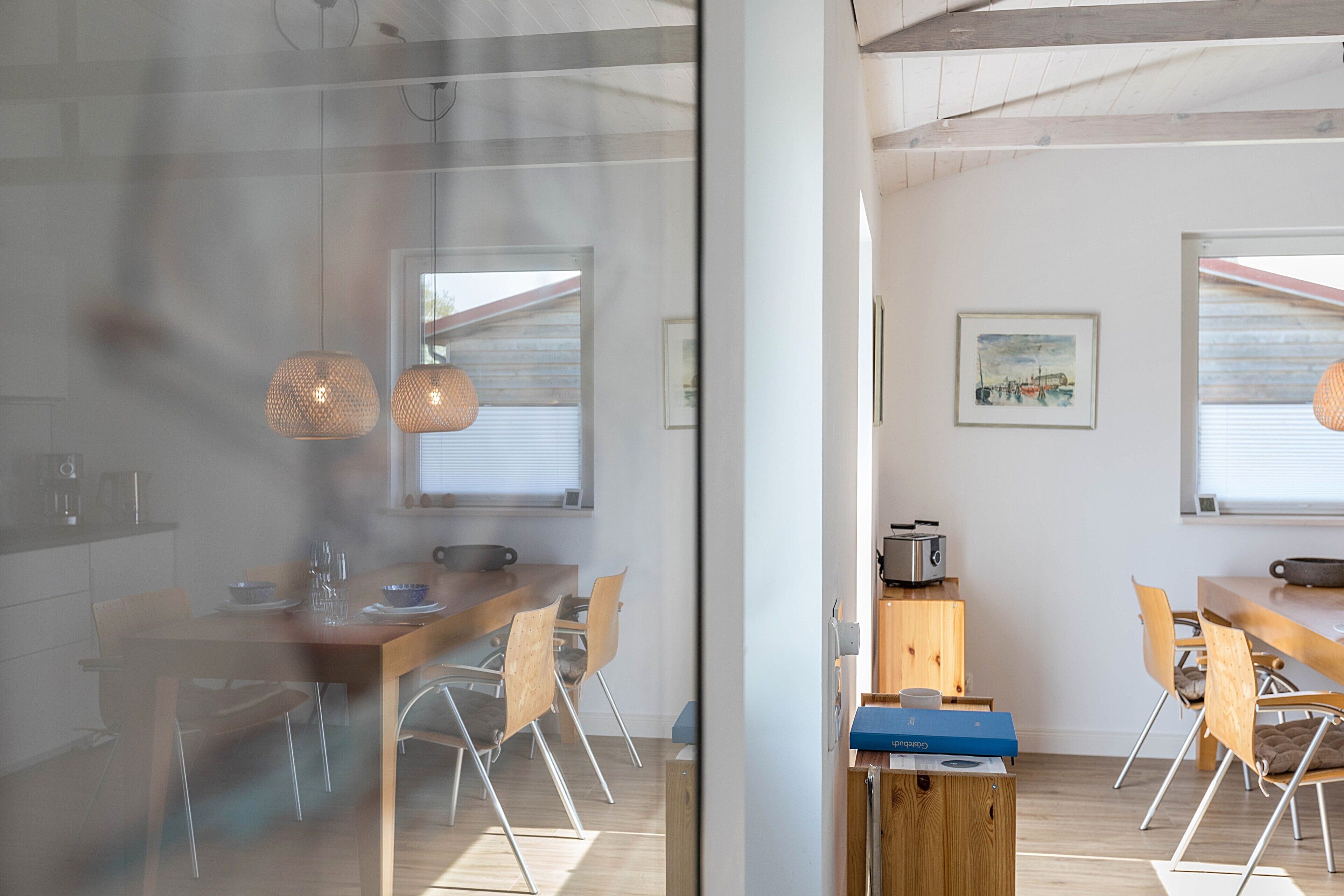 A modern kitchen with wooden cabinets, a dining table, and pendant lights.