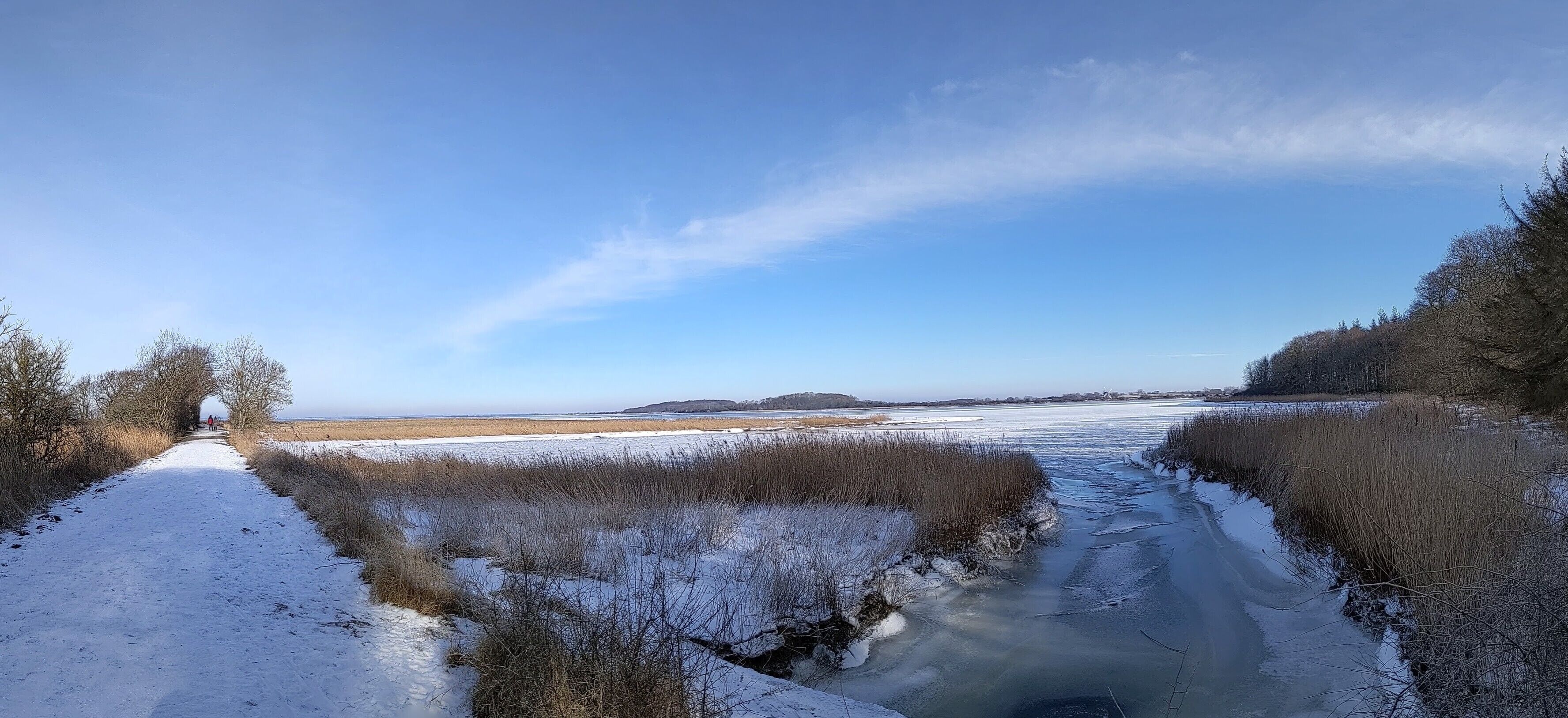 A snow-covered landscape with a frozen river, a clear sky, and distant hills.