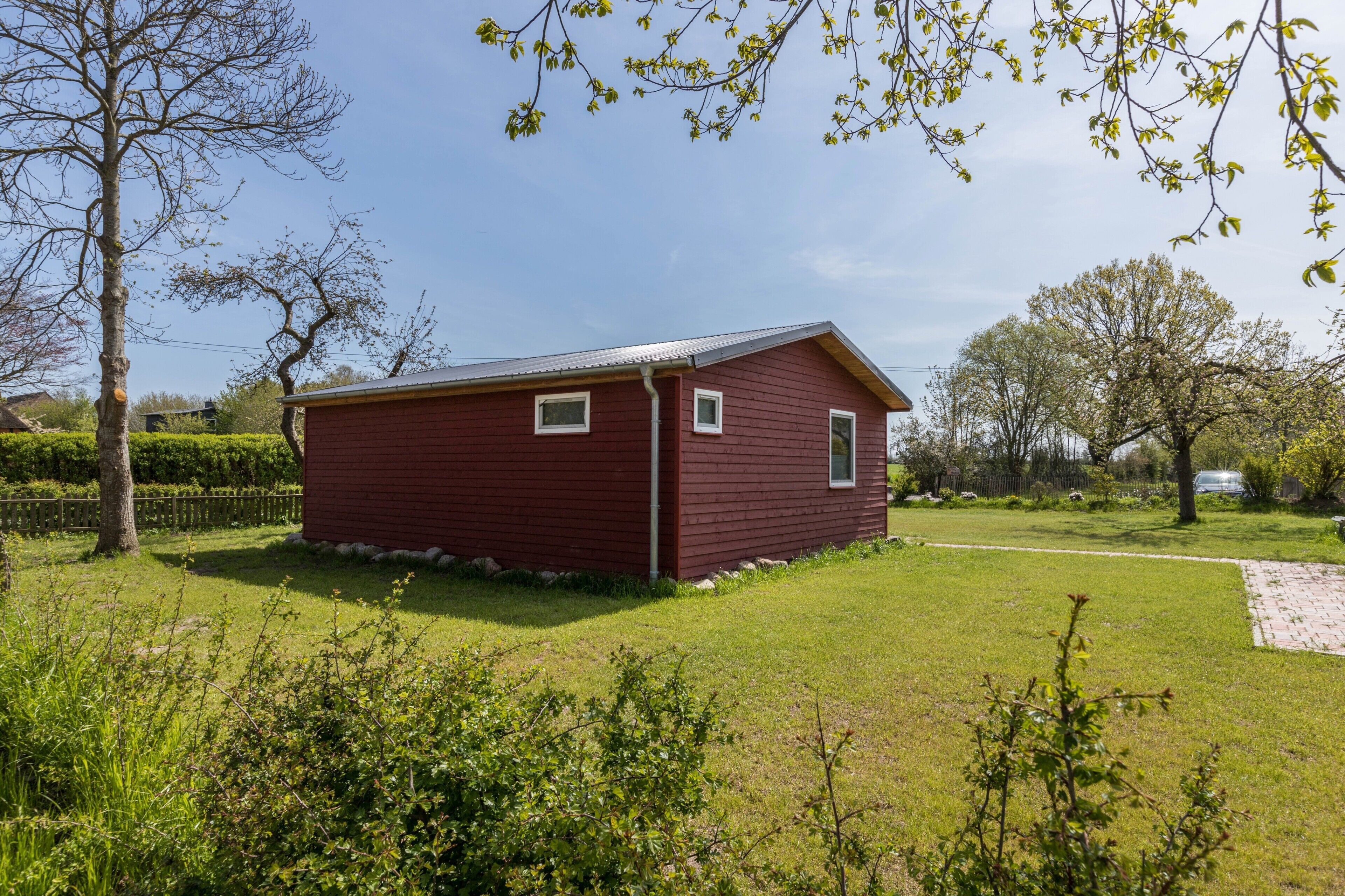 A red wooden building with a sloped roof, surrounded by a grassy yard and trees.
