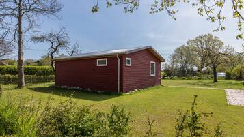 A red wooden building with a sloped roof, surrounded by a grassy yard and trees.
