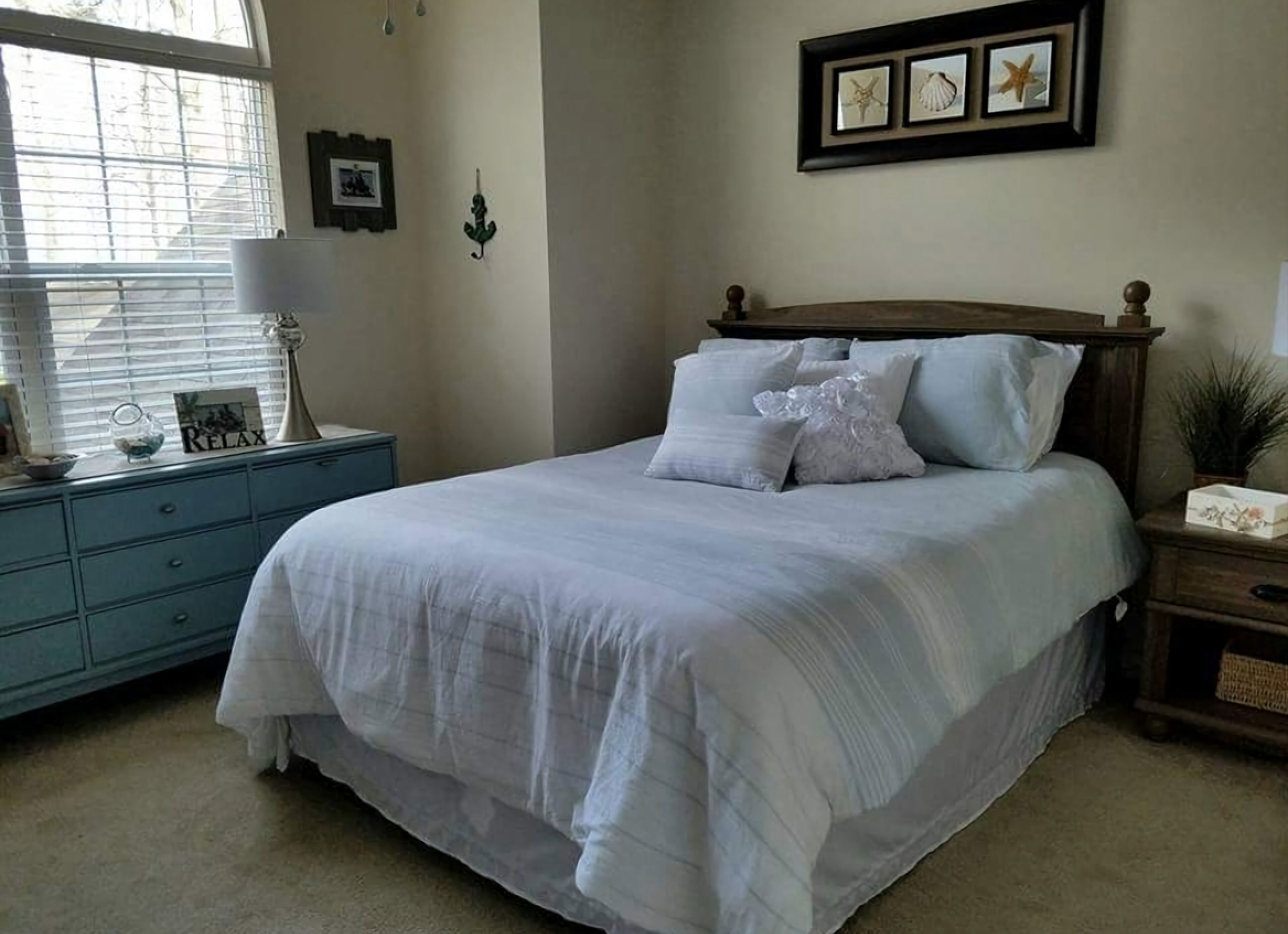 A bedroom with a large bed, a nightstand, a dresser, and a window with blinds.