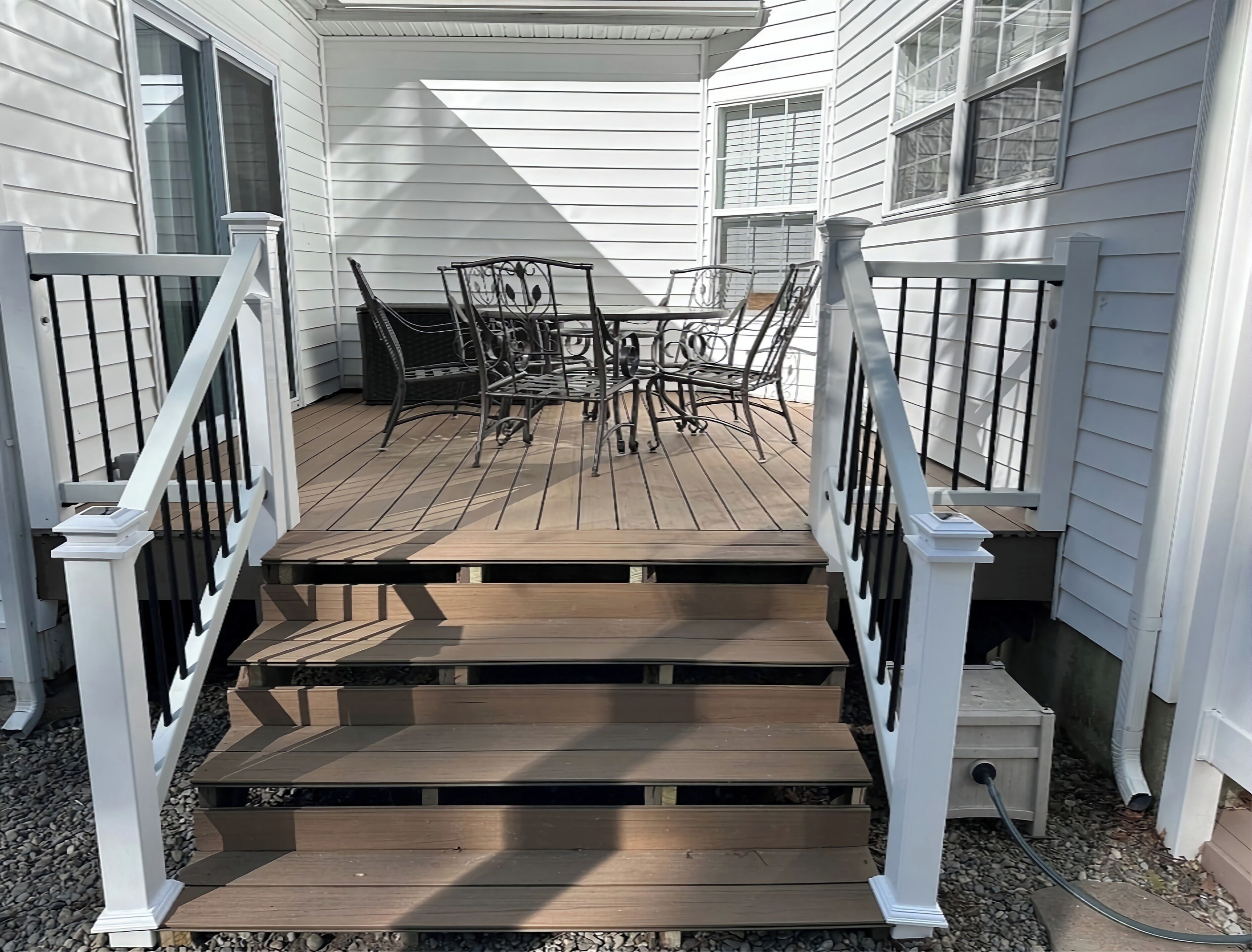 Une terrasse en bois avec une balustrade blanche qui mène à un patio couvert, aménagé avec une table et des chaises.