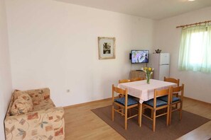Uma sala de estar pequena com um sofá, uma mesa de jantar com cadeiras, uma televisão e um frigorífico.