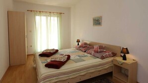 A bedroom with a bed, two bedside lamps, a window with curtains, a door, and a small painting on the wall.
