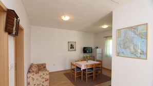 A room with a dining table, chairs, a sofa, a television, a refrigerator, and a map on the wall.