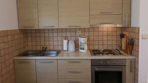 A kitchen with light wood cabinets, a stainless steel sink, a coffee maker, and a stove.