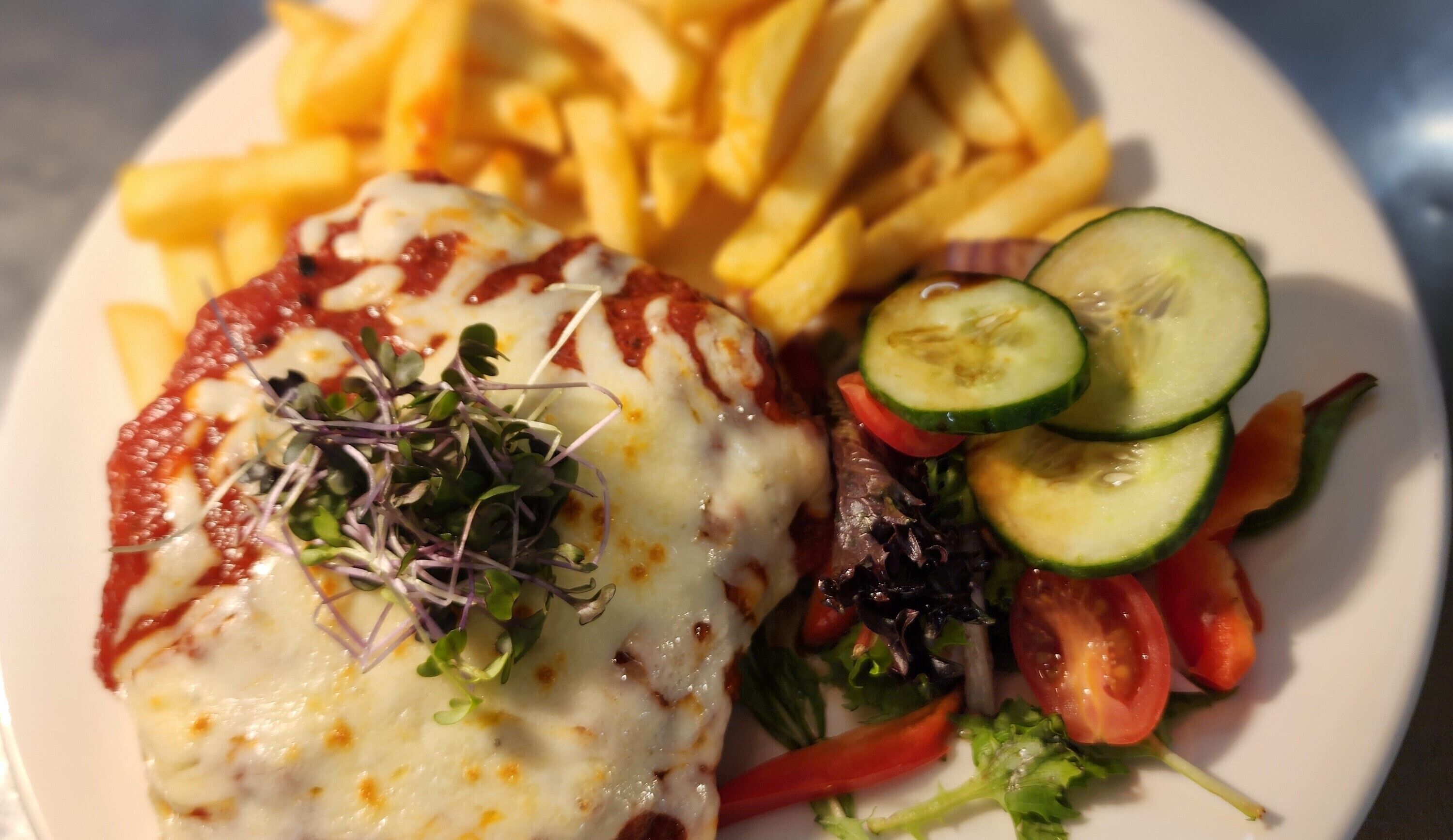 A plate with a chicken breast topped with melted cheese, a side of French fries, and a mixed vegetable salad.
