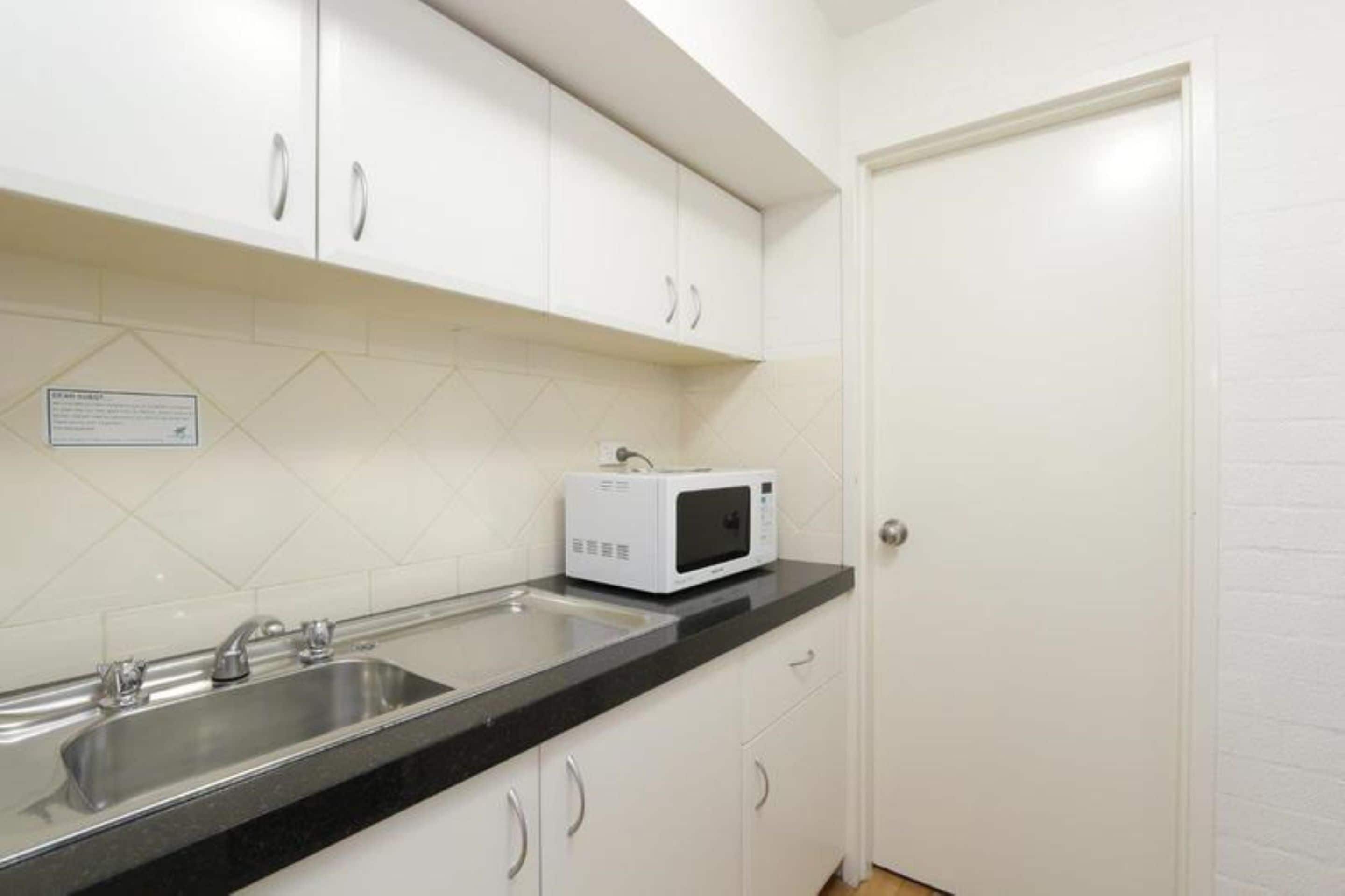 A kitchen with white cabinets, a black countertop, a stainless steel sink, and a white microwave.