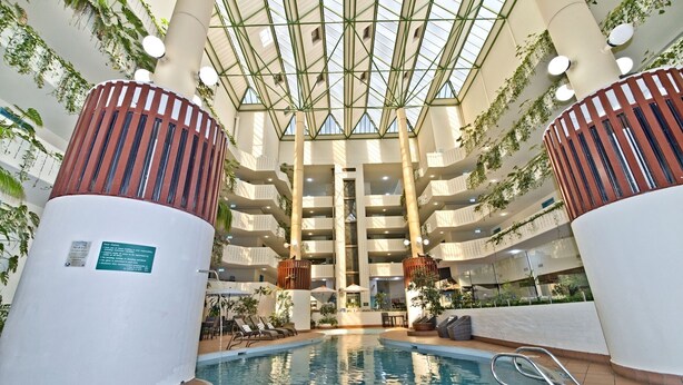 Un espace piscine intérieur à plusieurs niveaux, avec une piscine centrale, entourée de terrasses et de balcons agrémentés de verdure.
