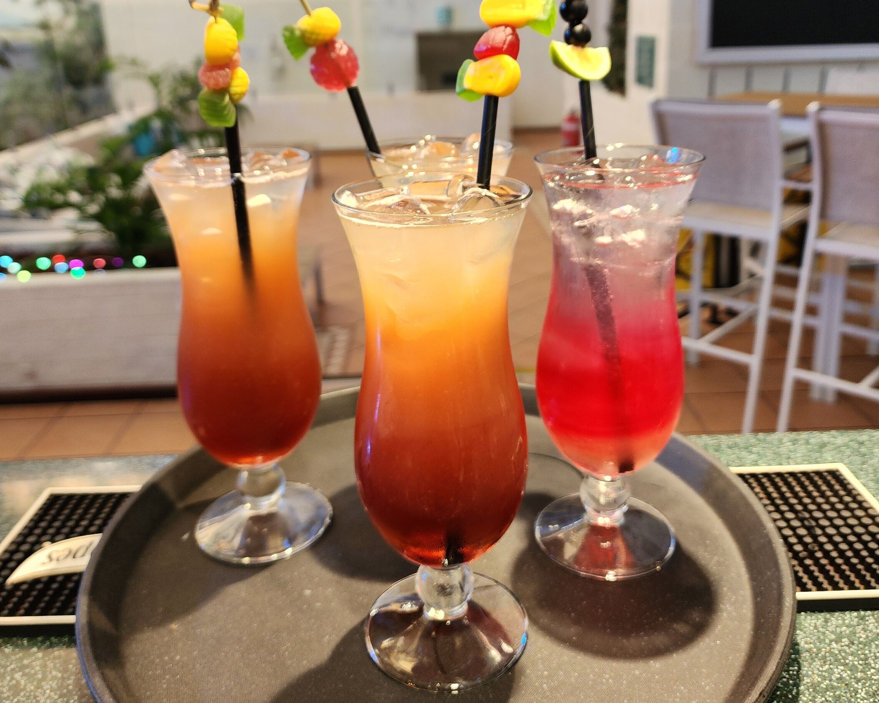 Three glasses of iced drinks on a tray with fruit skewers.