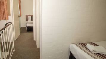 A narrow hallway with a bed on the right and a bathroom visible in the distance.