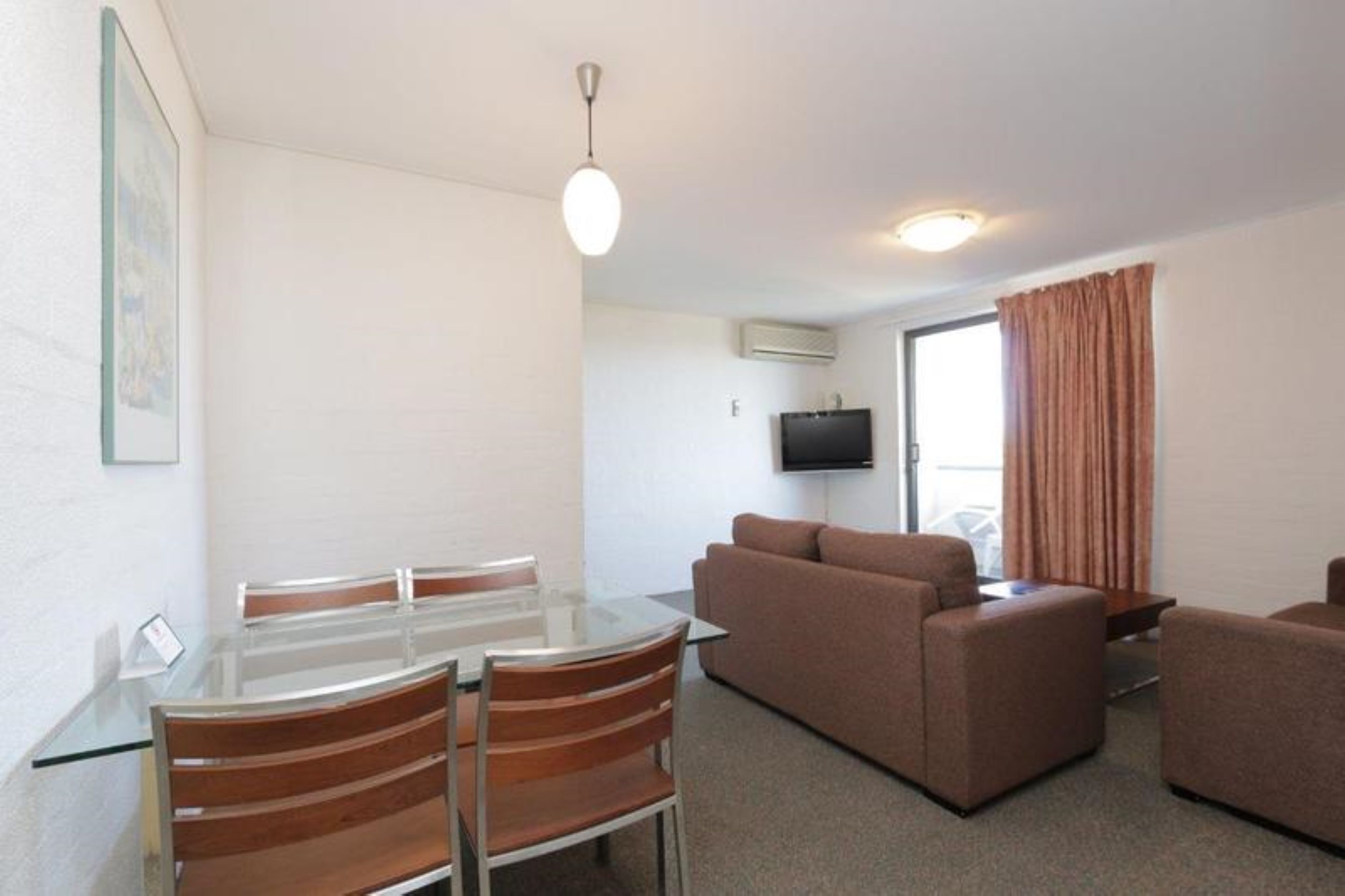 A compact living space with a glass dining table, two sofas, a flat-screen TV, and a sliding door.