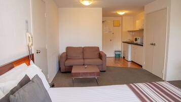 A compact hotel room with a bed, a sofa, a small table, and a kitchenette.