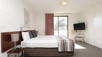 Habitación de hotel con cama, televisión, lámpara, un cuadro y ventana con cortinas.