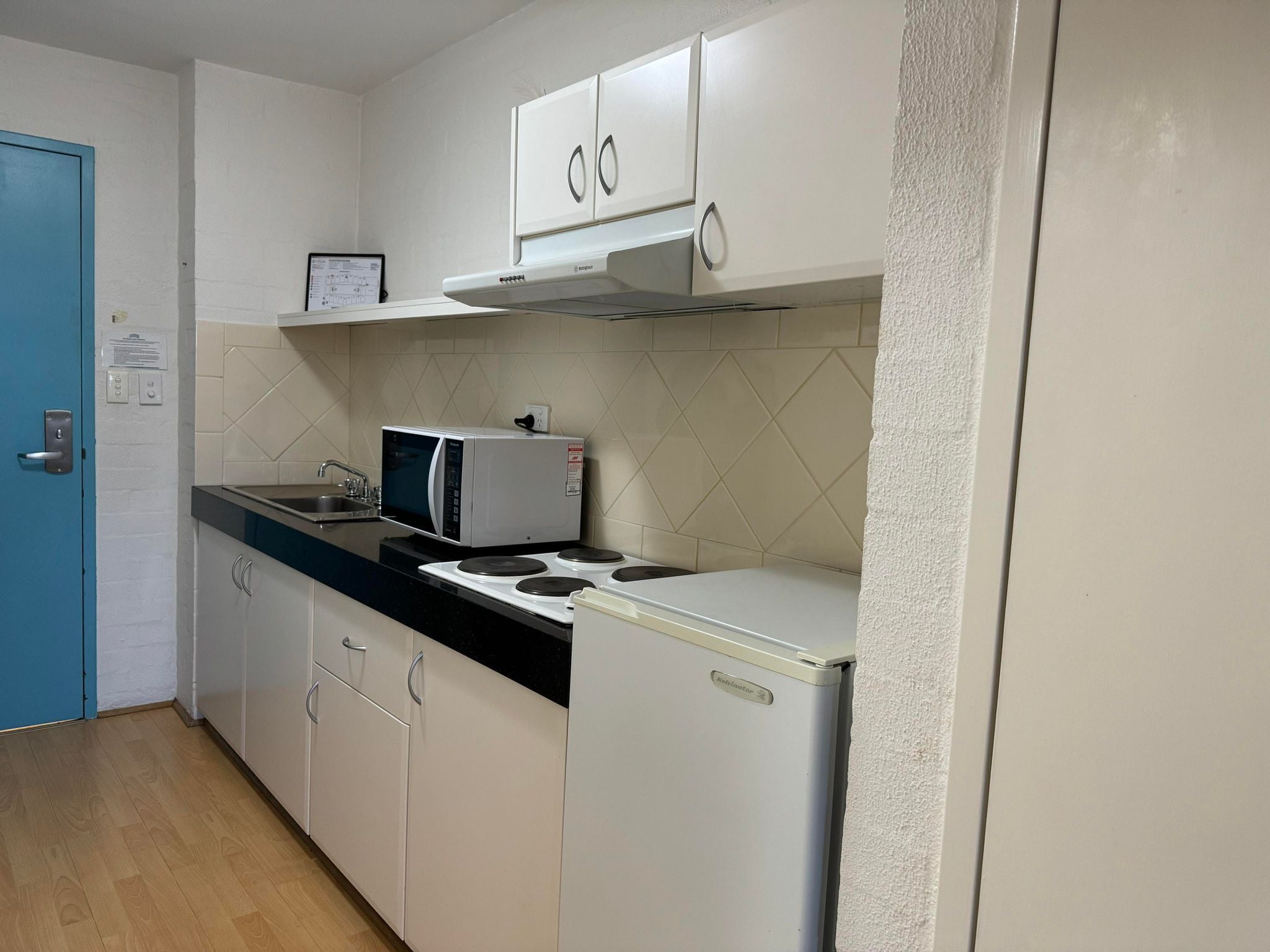 A compact kitchen with white cabinets, a microwave, a stove, and a refrigerator.