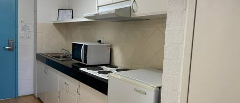 A compact kitchen with white cabinets, a microwave, a stove, and a refrigerator.