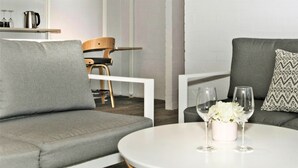 Un salon moderne avec un canapé gris, une table ronde blanche agrémentée d’un vase et de verres, et une chaise en bois.