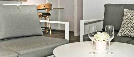 A modern living room with a grey sofa, a round white table with a vase and glasses, and a wooden chair.
