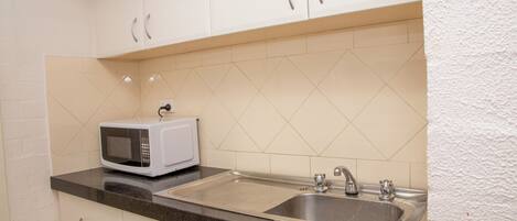 A kitchen with white cabinets, a black countertop, a white microwave, and a stainless steel sink.
