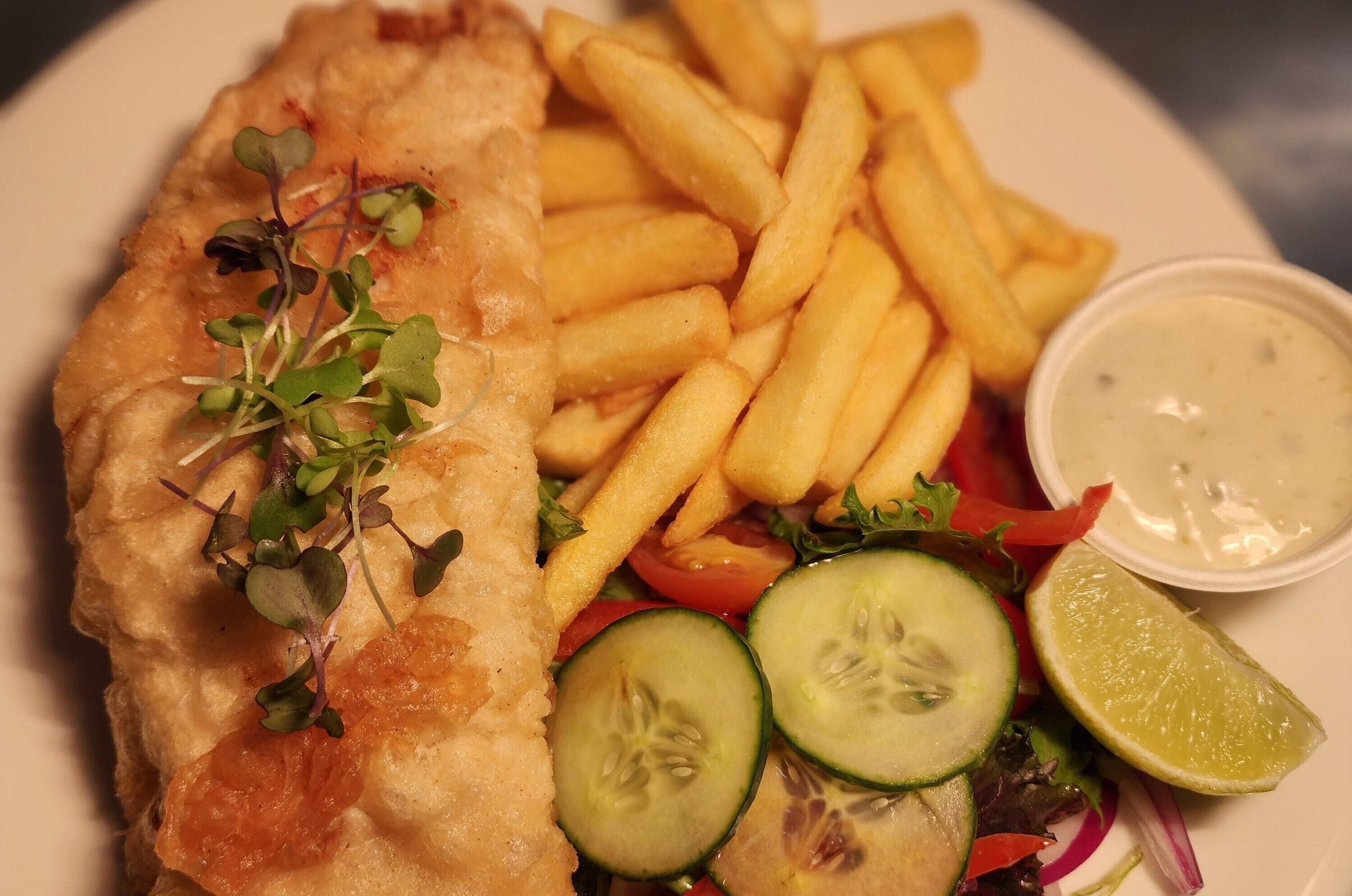 Un plato con pescado y papas fritas, ensalada y un recipiente pequeño con salsa.