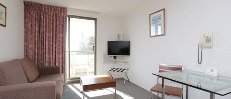 A hotel room with a sofa, a glass table with chairs, a television, a telephone, and a window with curtains.