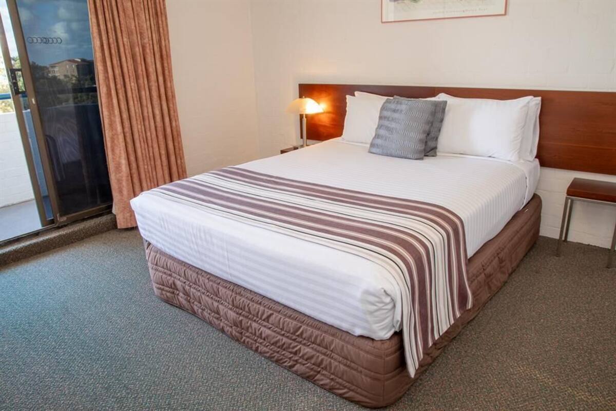 A hotel room with a large bed, a nightstand, a lamp, and a window with curtains.