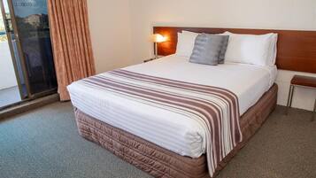 Una habitación de hotel con una cama grande, una mesita de noche, una lámpara y una ventana con cortinas.